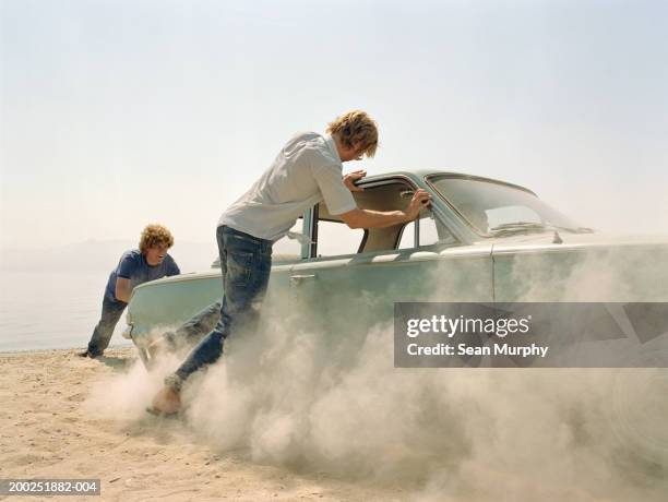 young men pushing car stuck in sand - stuck - fotografias e filmes do acervo