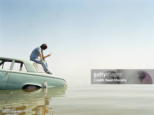 young man with mobile phone sitting on roof of car in water - car top down stock pictures, royalty-free photos & images