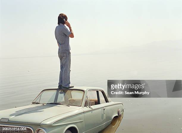 young man with mobile phone standing on roof of car in water - sunken car bildbanksfoton och bilder