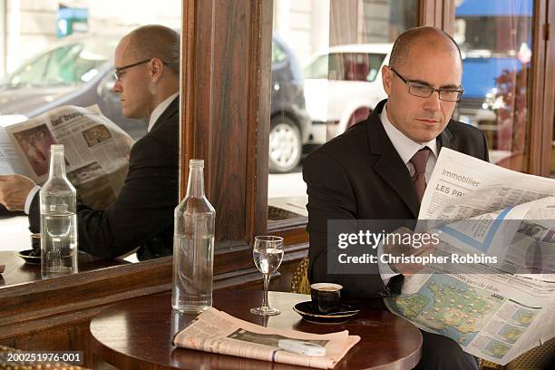 mature businessman sitting outside cafe reading newspaper - plano stockfoto's en -beelden