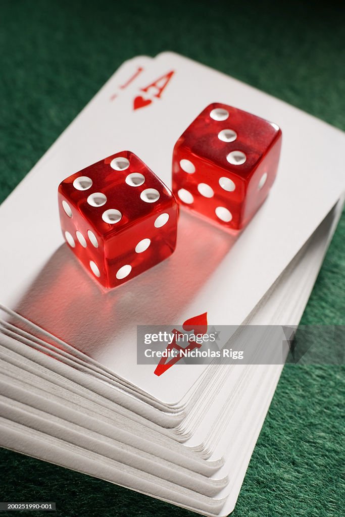 Red dice on pile of playing cards, close-up