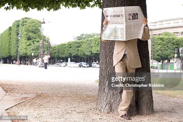 france, paris, man leaning on tree holding newspaper, obscuring face - 2005 fotografías e imágenes de stock