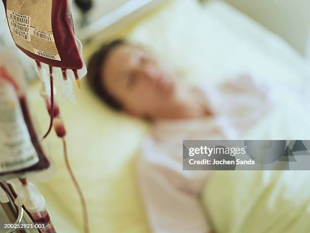 woman in hospital bed by iv drip filled with blood (focus on drip) - blood bag stock pictures, royalty-free photos & images