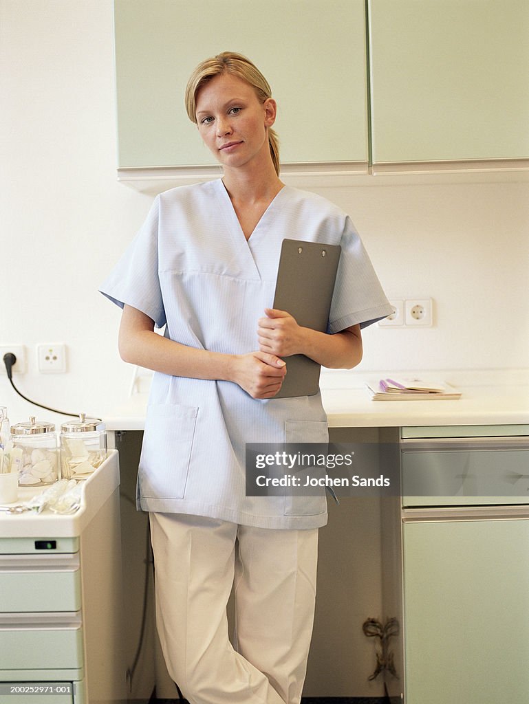 Young female nurse holding clipboard in kitchen, portrait