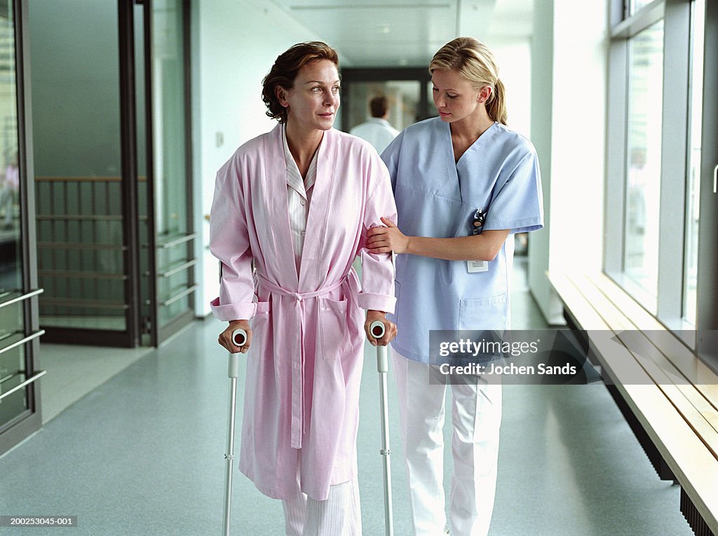 Female nurse holding patient using crutches in hospital corridor