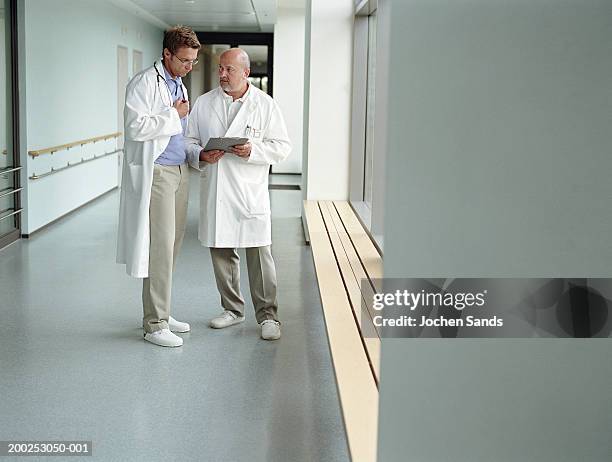 two mature male doctors talking in hospital corridor - two doctors talking stockfoto's en -beelden