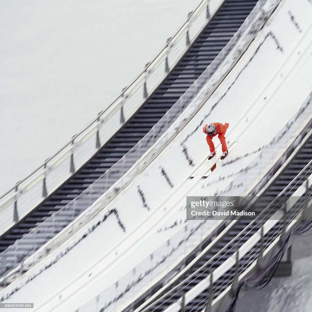 Ski jumper skiing down ramp, approaching jump