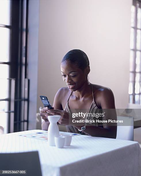young woman sending text message via mobile phone in restaurant - african american restaurant texting stockfoto's en -beelden