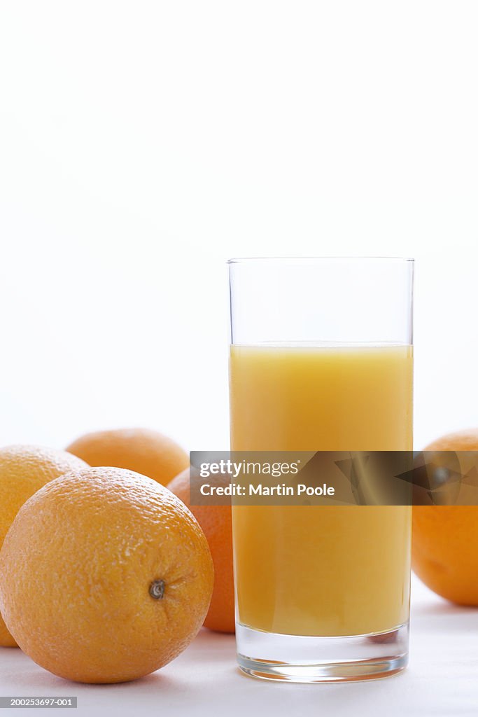 Whole oranges by orange juice in glass, close-up