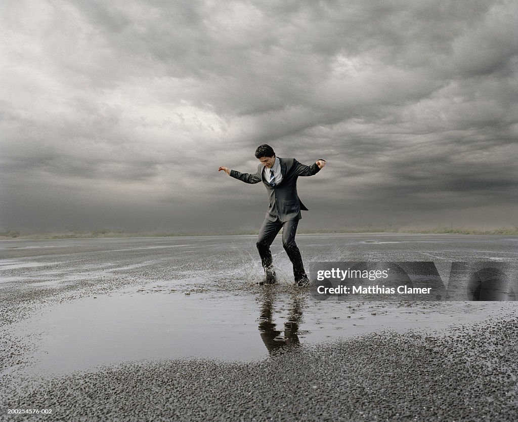 Businessman standing in puddle of water, arms stretched out