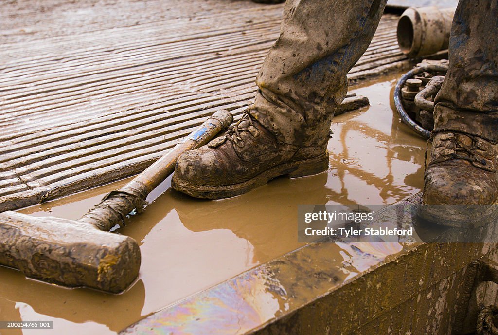 Workman standing on oil drilling platform, low section