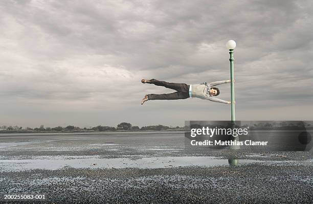 man holding on to lamp post in mid air, portrait - face wind photos et images de collection