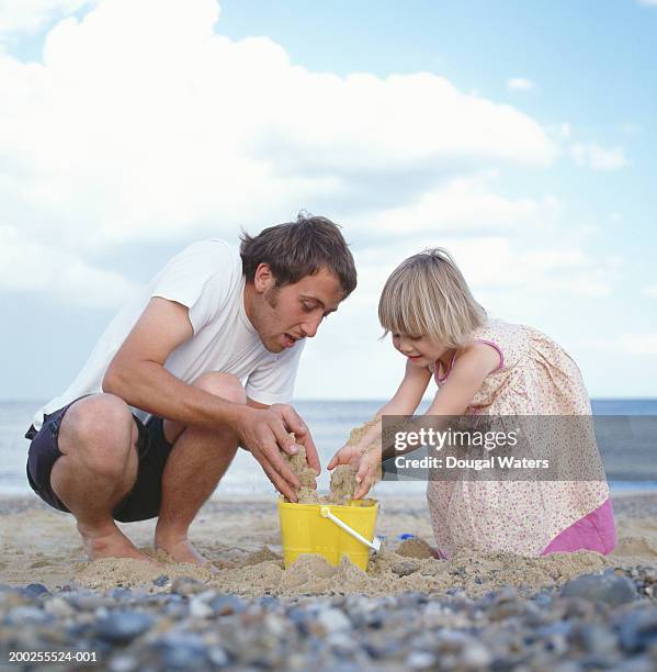 father and daughter (2-5) pouring sand into bucket on beach - white dress stock pictures, royalty-free photos & images