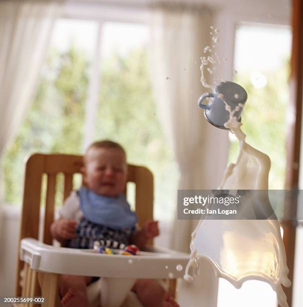 baby boy (6-9 months) in high chair, cup of milk flying in air - spilt milk foto e immagini stock