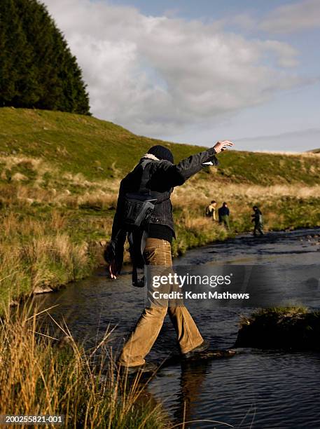 man balancing on rocks in stream, three men in background - llyn brianne reservoir stock pictures, royalty-free photos & images