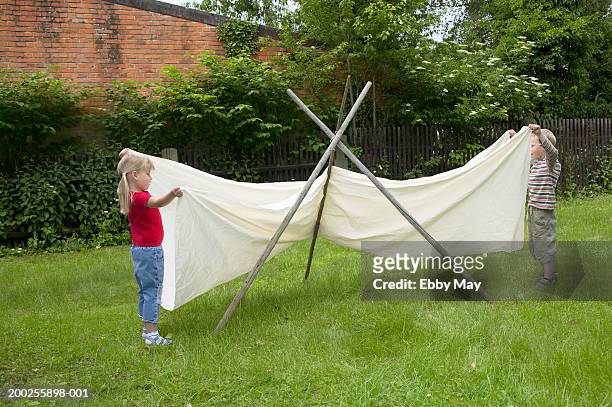 boy and girl (4-6) building teepee in garden - tipi stock-fotos und bilder