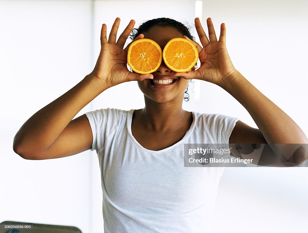 Teenage girl (15-17) holding orange slices in front of eyes