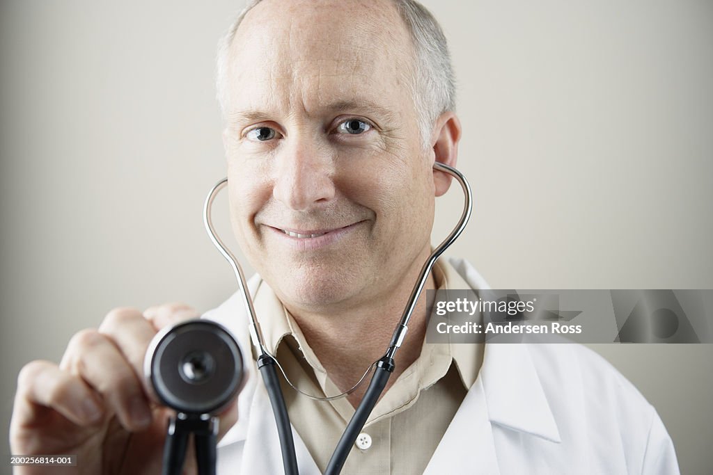 Mature male doctor using stethoscope, smiling, portrait