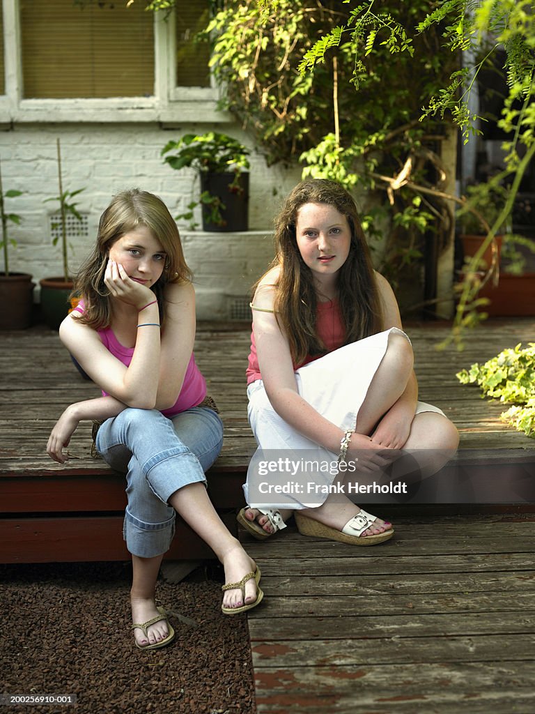 Two teenage girls (13-15) sitting on garden decking, portrait