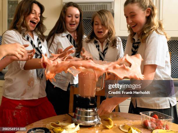 teenage girls (13-15) in kitchen, milkshake exploding from blender - verschütten stock-fotos und bilder