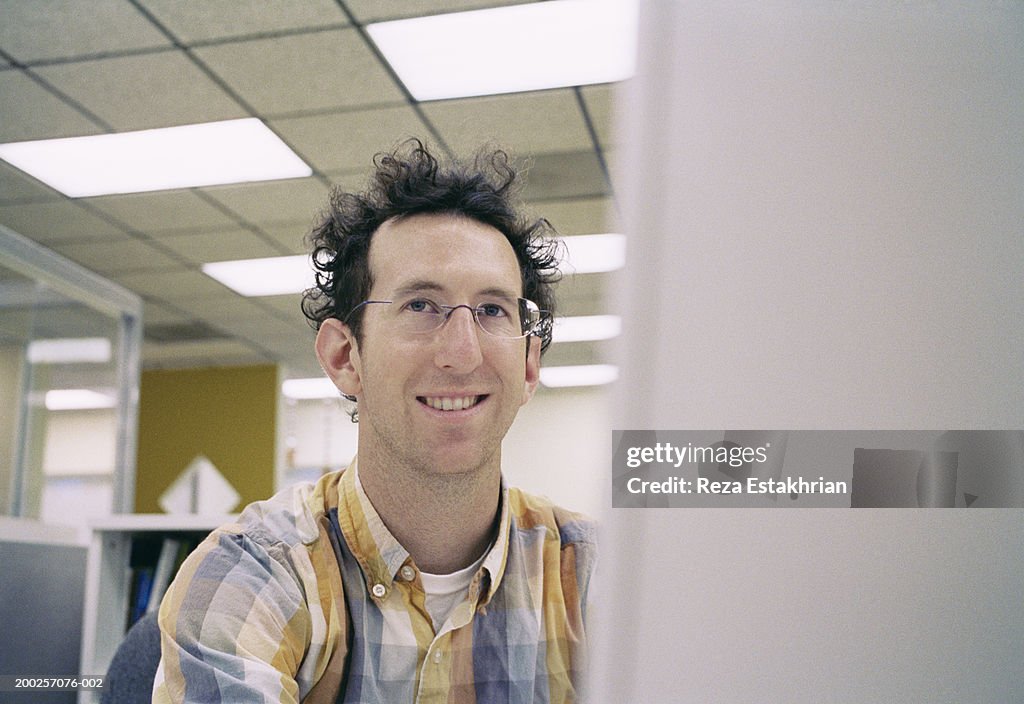Businessman sitting in front of computer monitor, smiling