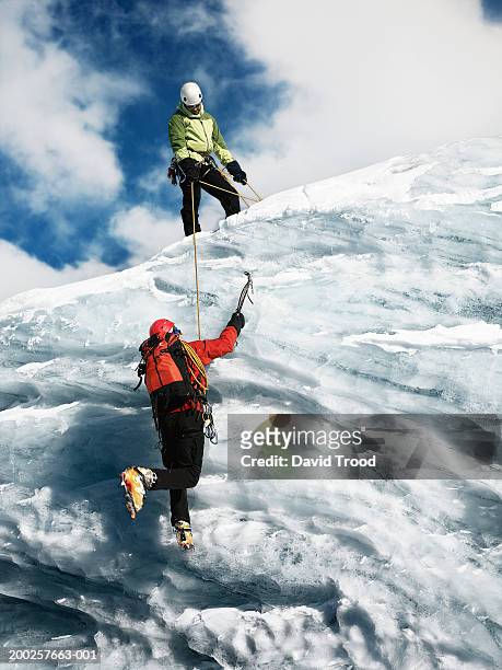 two male mountain climbers, one holding rope to help other ascend - berg klimmen team stockfoto's en -beelden