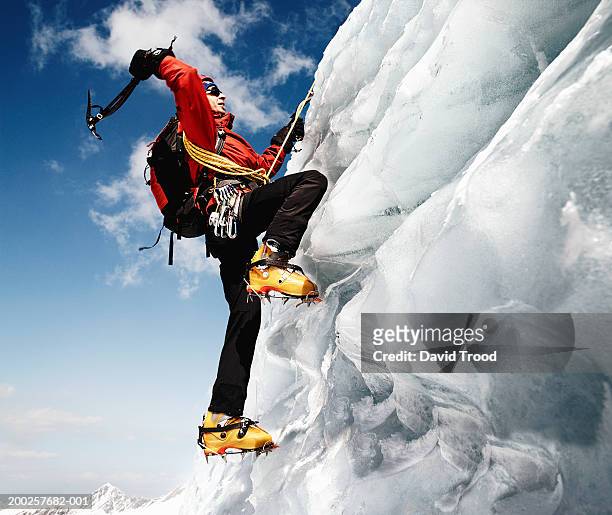 male mountain climber on ice-covered rock face, low angle view - crampon stock-fotos und bilder