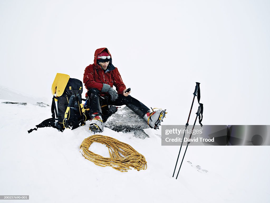 Male mountain climber sitting on rock, looking at mobile phone