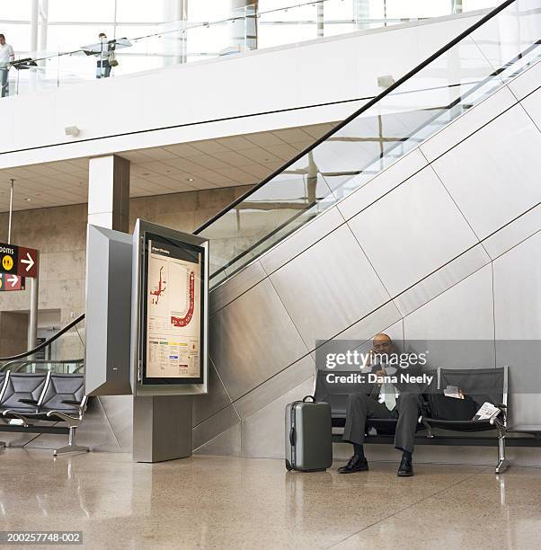 businessman sitting in airport, using mobile phone, looking at watch - airport frustration stock pictures, royalty-free photos & images