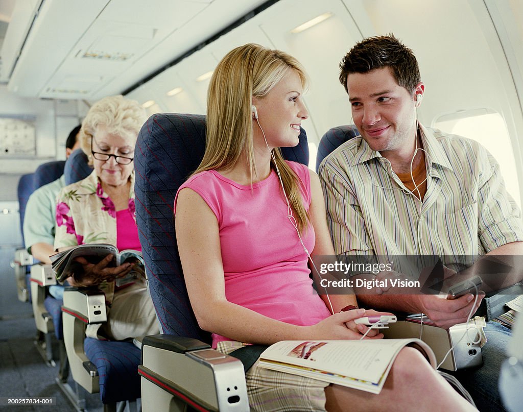 Couple sitting on plane wearing MP3 players, smiling