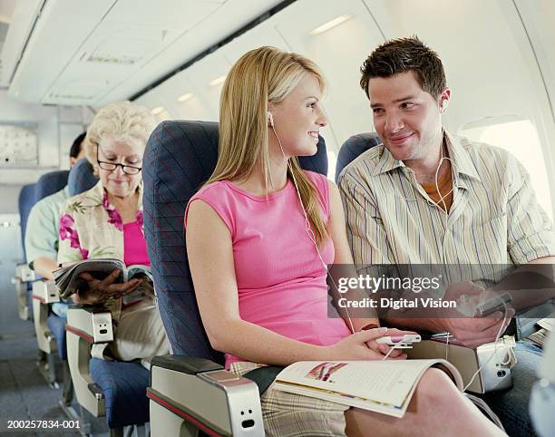 couple sitting on plane wearing mp3 players, smiling - couple airplane stock pictures, royalty-free photos & images