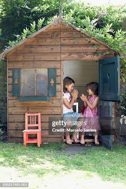 two sisters (4-7) playing in wendy house in garden, smiling - playhouse stockfoto's en -beelden