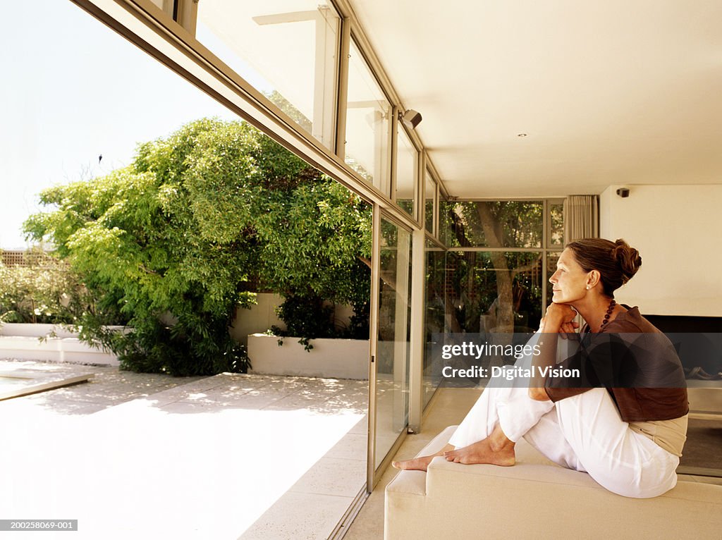 Mature woman sitting on sofa by balcony indoors, side view