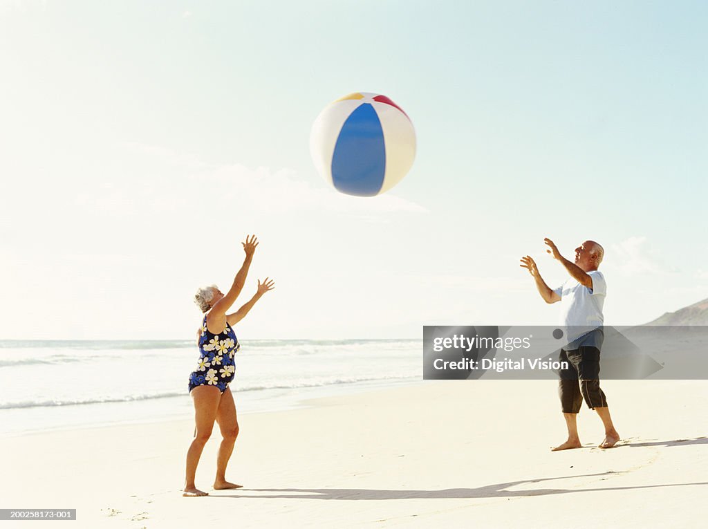 Senior couple throwing beach ball on beach