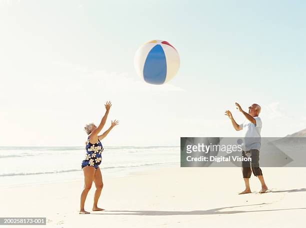 senior couple throwing beach ball on beach - alte frau badeanzug stock-fotos und bilder