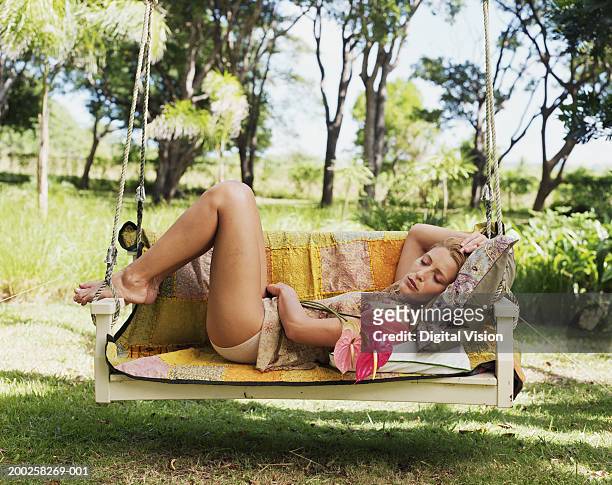 young woman relaxing on swing chair, holding flower, eyes closed - hollywoodschaukel stock-fotos und bilder