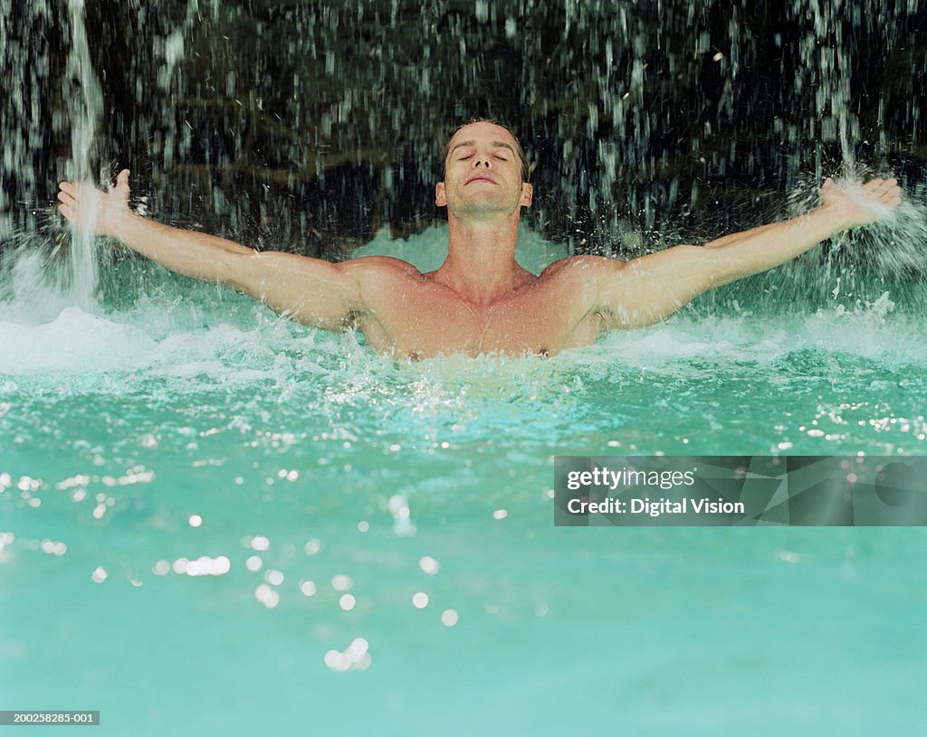 Man in water with outstretched arms, falling water splashing off hands