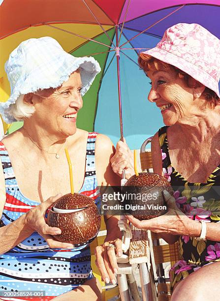 two senior women holding coconuts, smiling at each other, close-up - 2 coconut drinks ストックフォトと画像