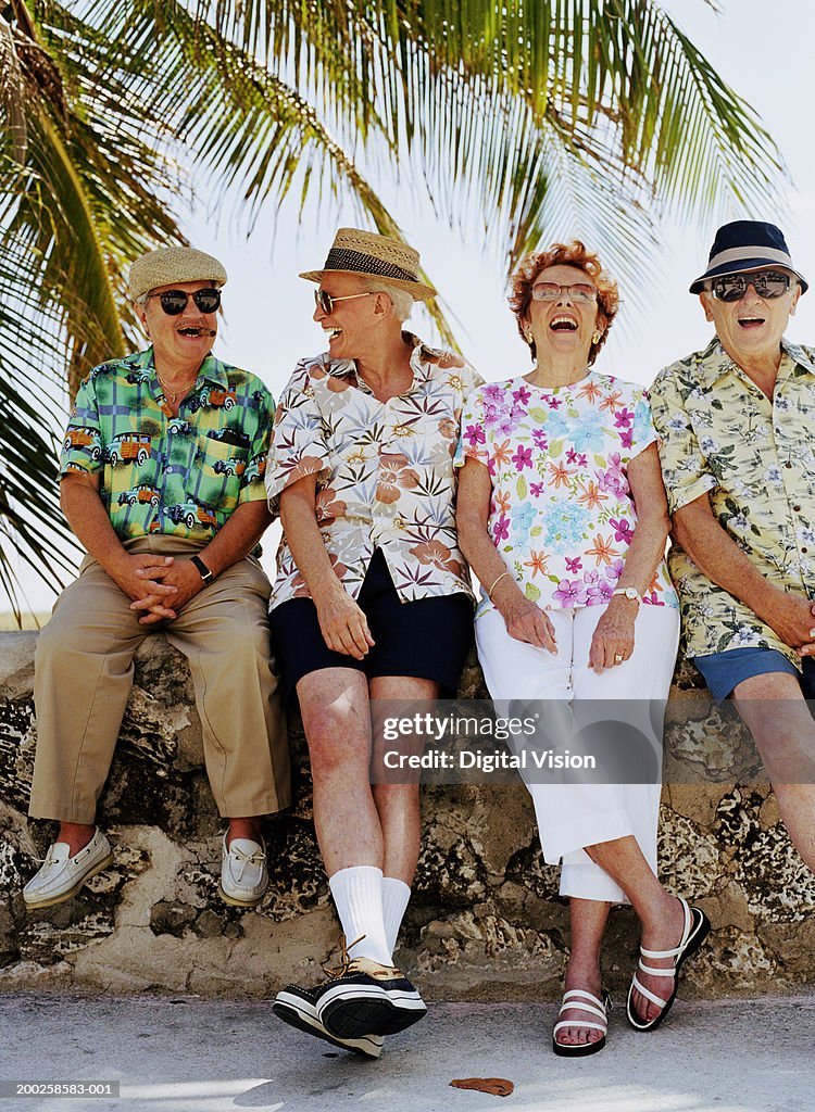 Group of four senior people sitting on wall outdoors, laughing