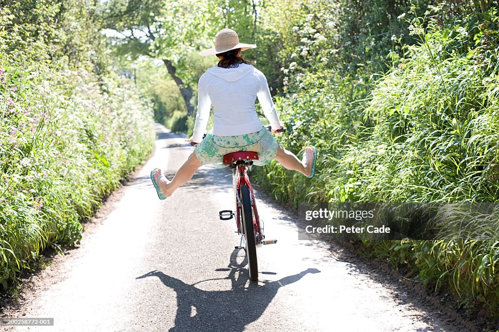Young woman on bicycle with legs spread open, rear view