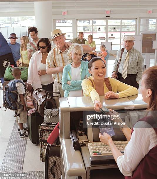 woman handing bank card to woman at airport check in desk, smiling - airport frustration stock pictures, royalty-free photos & images