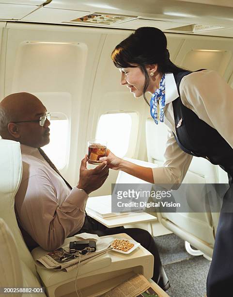air stewardess handing drink to male passenger, smiling - airline service foto e immagini stock
