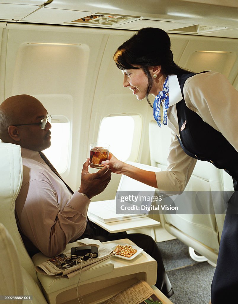 Air stewardess handing drink to male passenger, smiling