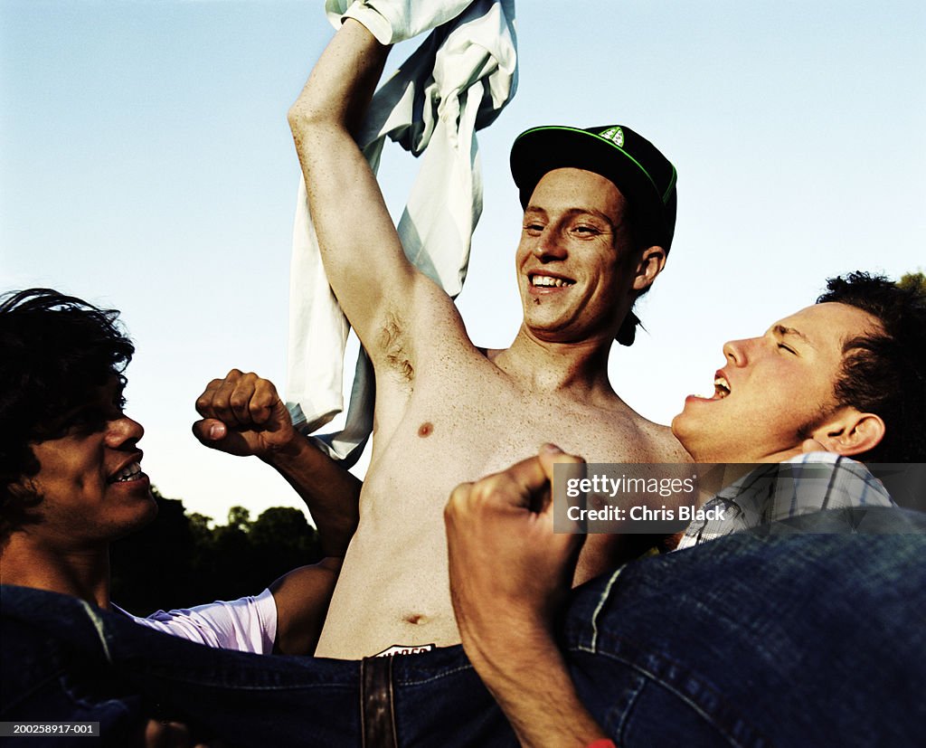 Two men holding up friend outdoors, celebrating