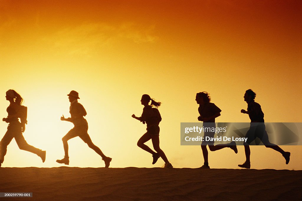 People running in desert at dusk, side view