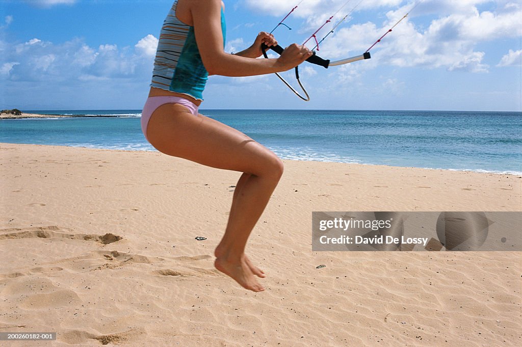 Female kiteboarder in mid-air on beach