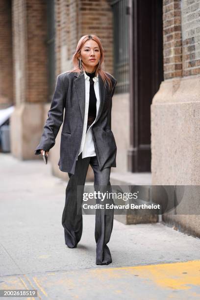Tina Leung wears earrings, a black turtleneck top, a white shirt, a gray oversized blazer jacket , flared pants, outside Proenza Schouler , during...