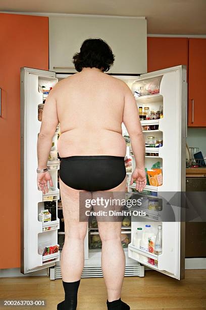 man wearing underwear, standing by open fridge, rear view - fat guy foto e immagini stock