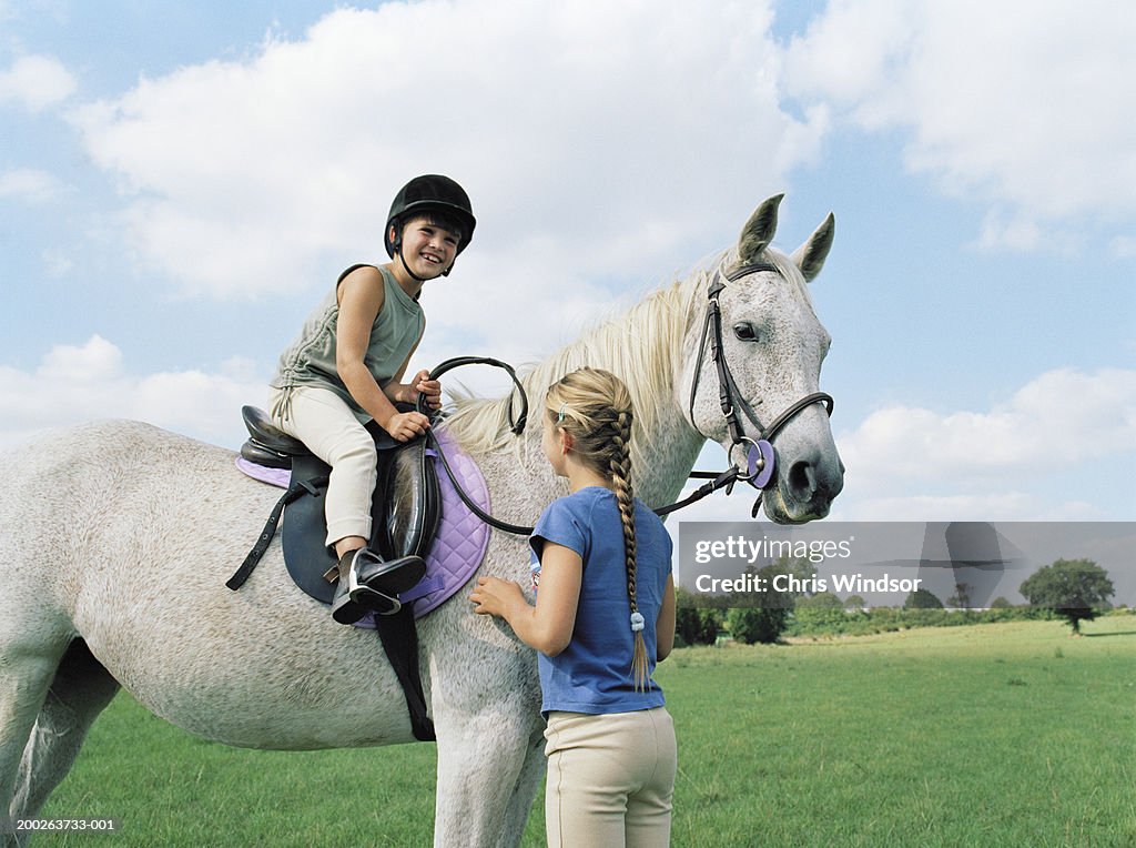 Girl (10-12) standing by sister (6-8) on horse, smiling