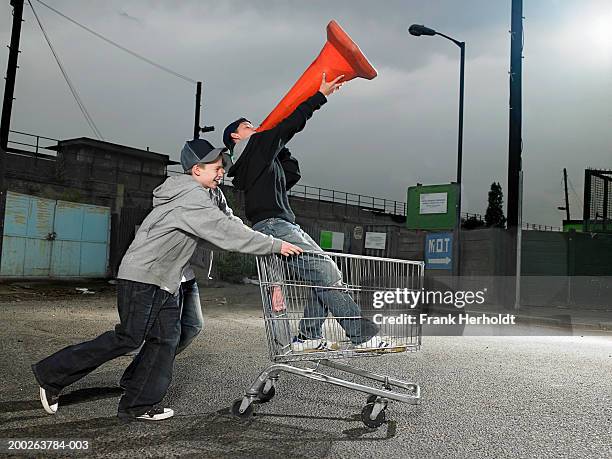 teenage boys (13-15) pushing friend holding traffic cone in trolley - alleen tienerjongens stockfoto's en -beelden